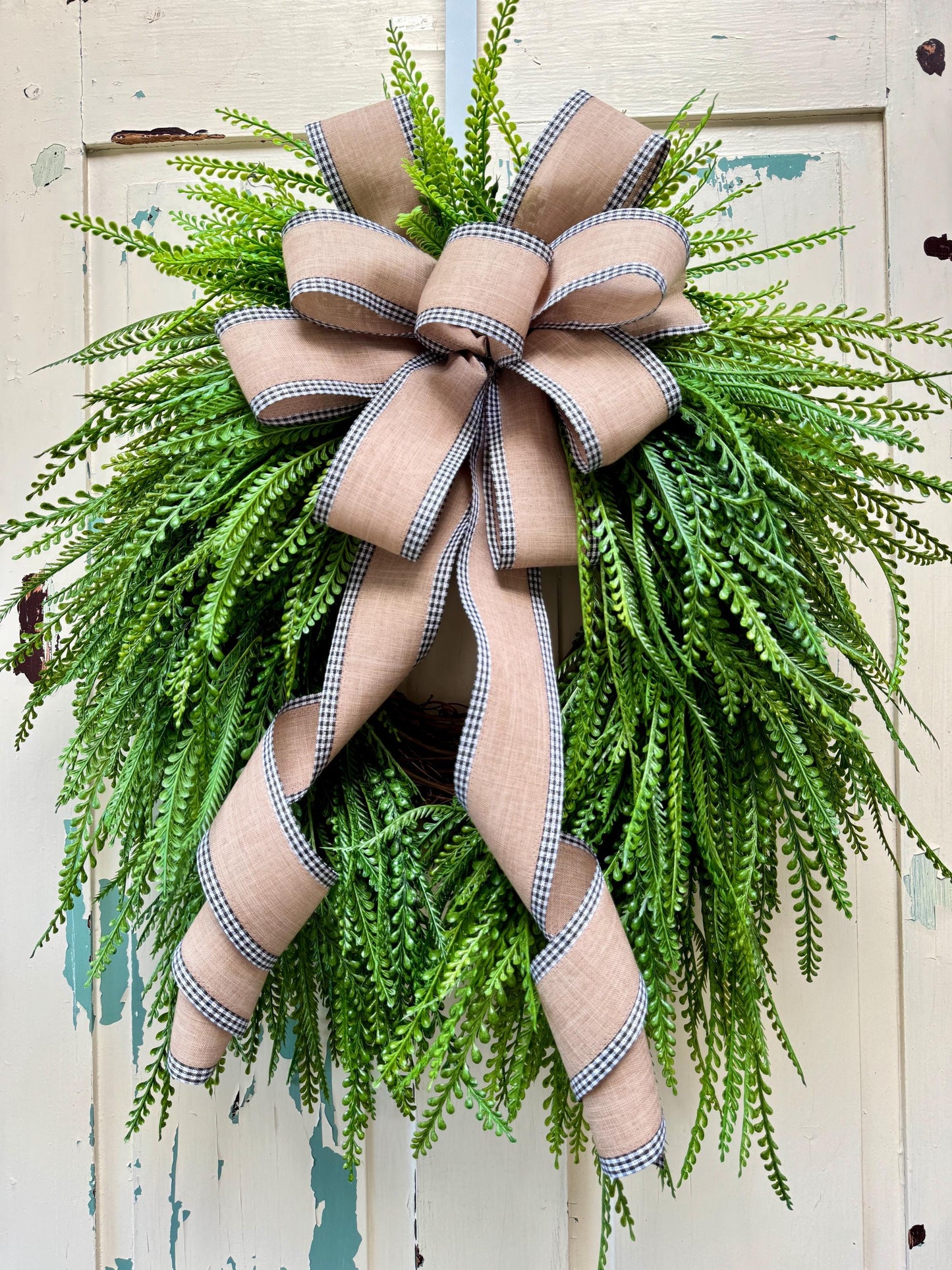 A beaded fern round wreath with a tan bow and black gingham edging